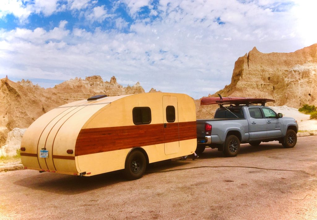 Wooden tear drop shaped camper being towed by a truck in the desert